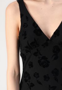 Μαύρο φόρεμα με λουλουδάτο μοτίβο, με βαθύ V-λαιμό και χωρίς μανίκια. Κατασκευασμένο από υφασμάτινη υφή, με ανάγλυφα σχέδια ρόδων.