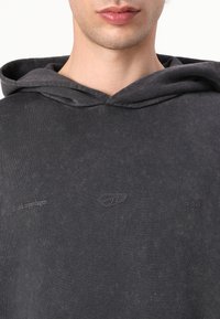 Mikina s kapucňou v tmavosivej bavlne, s textúrovaným povrchom, embossovaným logom a minimalistickým dizajnom s uvoľneným strihom.