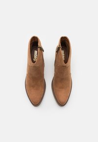 Botas de ante marrón hasta el tobillo con cremalleras laterales, punteras afiladas y suelas marrón oscuro, vistas desde arriba sobre un fondo blanco.