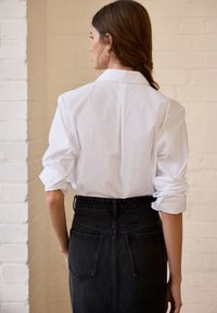 Vit skjorta med uppvikta ärmar, med klassisk krage och veck bak, tillsammans med en högmidjad svart denimkjol med två bakfickor.
