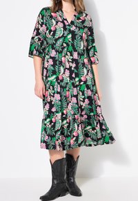 Robe noire avec des motifs floraux et de feuilles en rose et vert. Dotée d'un col en V, de manches trois-quarts et d'un ourlet en couches. Portée avec des bottes de cow-boy noires.