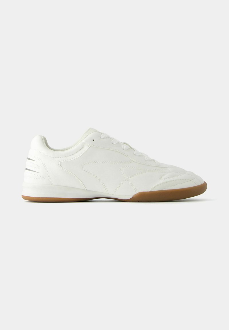 Białe sneakersy z gładką skórzaną cholewką, teksturowanymi wzorami po bokach i brązową gumową podeszwą. Posiadają sześć oczek i okrągły czubek.