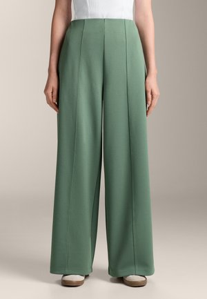 Pantalon large en tissu vert doux, avec des coutures verticales et une texture lisse, complété par une taille haute.