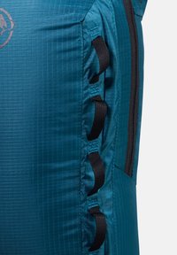 Εγγύς λήψη της πλευράς ενός τυρκουάζ σακιδίου με μαύρες υφασμάτινες θηλιές και έναν κατακόρυφο μαύρο φερμουάρ στη δεξιά άκρη.