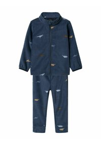 Ensemble de pyjama en polaire bleu marine avec une veste zippée et un pantalon, arborant de petits motifs de dinosaures en beige et bleu clair. Texture douce.