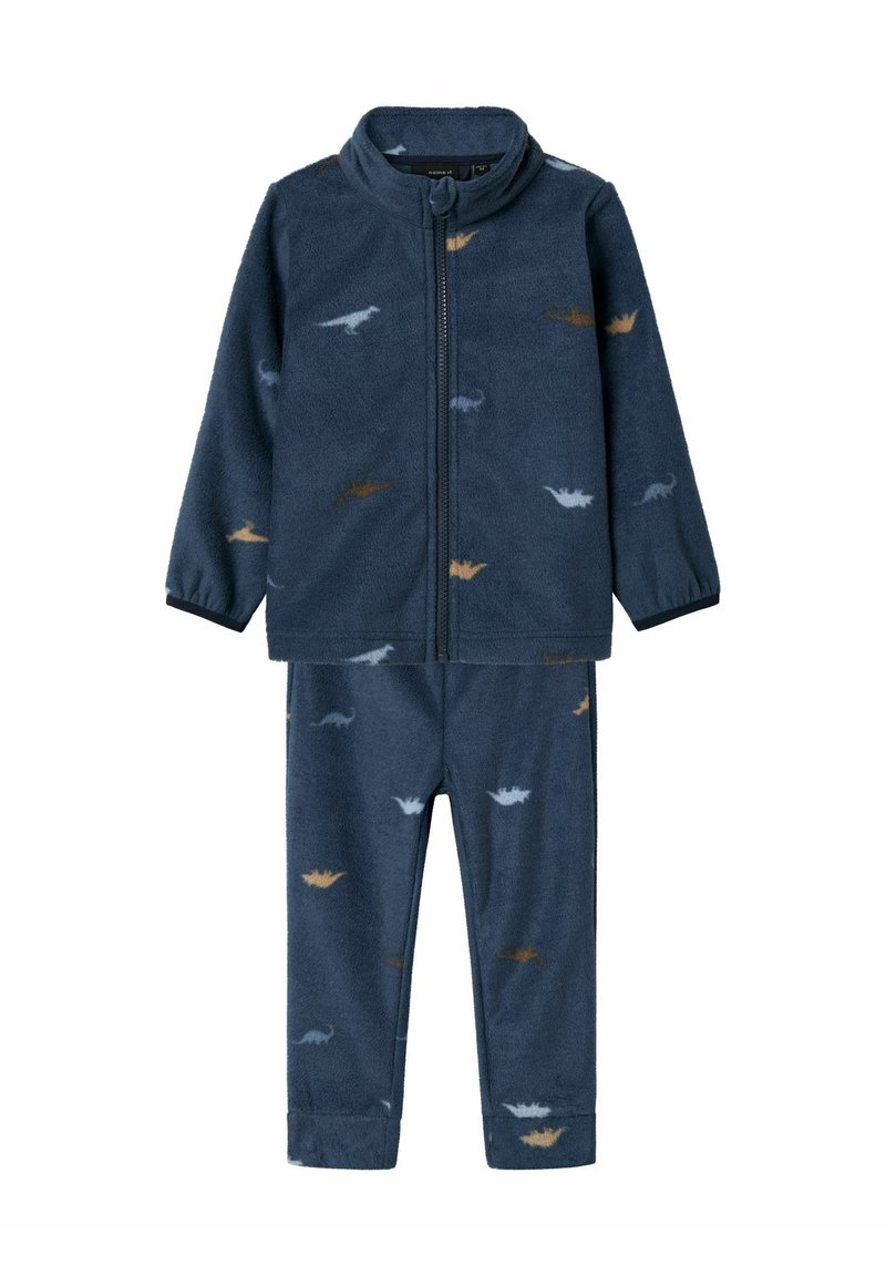 Ensemble de pyjama en polaire bleu marine avec une veste zippée et un pantalon, arborant de petits motifs de dinosaures en beige et bleu clair. Texture douce.