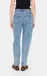 Svijetloplave traperice s opuštenim krojem, vidljivim stražnjim džepovima i etiketom na pojasu. Blago izbljedjela tekstura i dizajn ravnih nogavica.