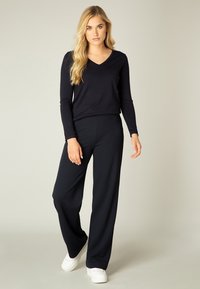 Marineblauwe longsleeve V-hals top gecombineerd met marineblauwe wijde broek en witte sneakers, met een soepele stof en een relaxte pasvorm.