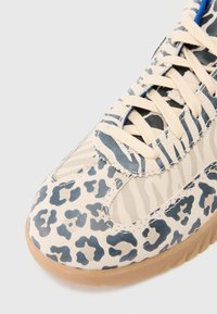 Baskets beige avec imprimé léopard bleu, dotées d'une tige en tissu texturé, de panneaux en filet, et d'une semelle en caoutchouc gomme avec des lacets et des détails de couture.
