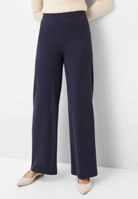 Wide-leg trousers in navy fabric with a smooth texture. Features a high waist and front pleats. Paired with beige pointed-toe shoes.