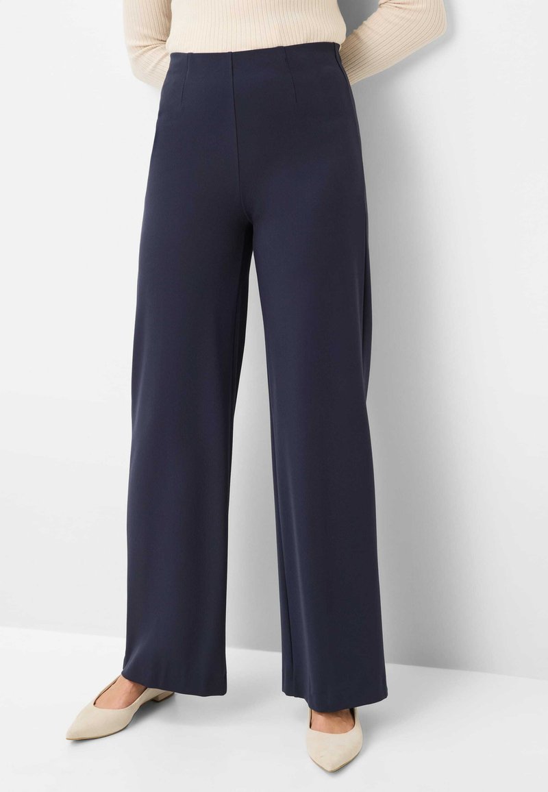 Wide-leg trousers in navy fabric with a smooth texture. Features a high waist and front pleats. Paired with beige pointed-toe shoes.
