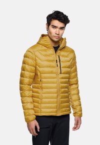 Gelbe gepolsterte Jacke mit Kapuze, ausgestattet mit horizontaler Steppung, einem Reißverschlusstaschen auf der Brust und elastischen Bündchen. Das Material wirkt glänzend und leicht.