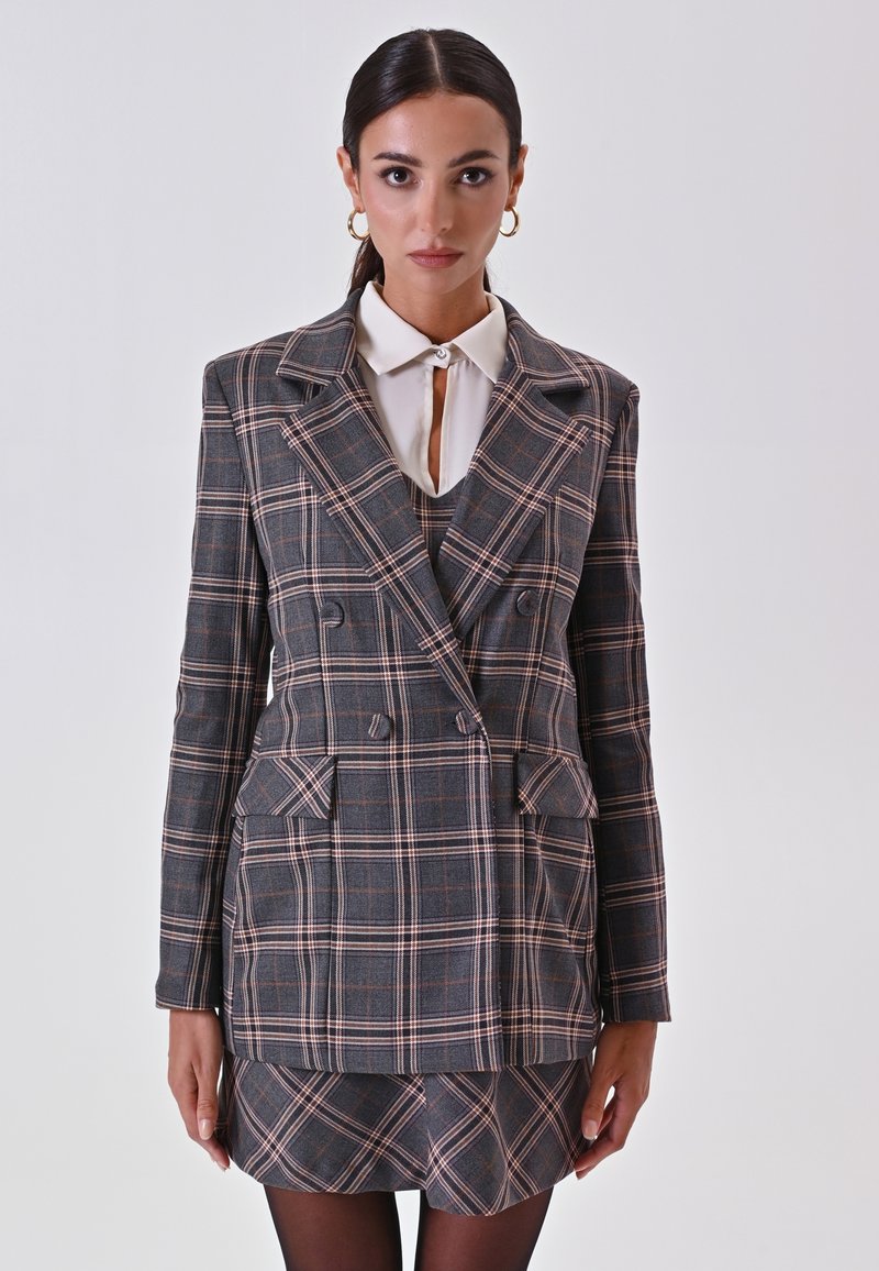 Donkergrijze dubbelreversible blazer met een roze en witte ruitpatroon, voorzien van brede revers, zakflappen en een aansluitende minirok.