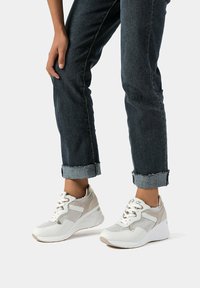 Sneakers bianchi e beige con pannelli in rete, lacci e suola a zeppa, abbinati a jeans blu scuro arrotolati con orli sfilacciati.