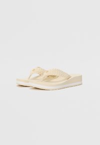 Beige flip-flops med et vævet strop, der har en struktureret fodseng og en platformssål med en hvid accentlinje.
