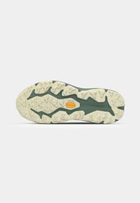 Semelle en caoutchouc verte présentant un motif texturé avec des crampons proéminents, contrastant avec un intermédiaire de couleur claire et un détail de logo jaune.