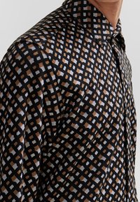 Zwart shirt met een geometrisch patroon van bruine, witte en zwarte vierkanten. Gestructureerde stof met een klassieke kraag en knoopsluiting.