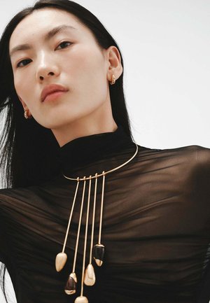 Collar de oro con cinco piedras pulidas colgantes sobre una blusa negra translúcida. Textura suave con un diseño minimalista y acentos metálicos.