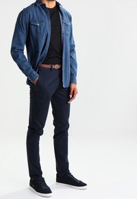 Denimskjorta, svart t-shirt, marinblå chinos, brun bälte och mörka sneakers. Skjortan har två bröstfickor och knäppning.