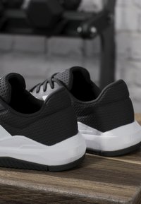 Chaussures de sport noires et blanches avec tissu texturé et semelles blanches épaisses reposant sur une surface en bois avec un arrière-plan flou.