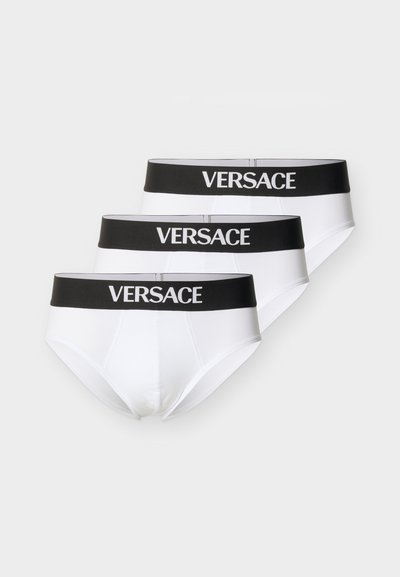 Trois slips blancs pour homme avec des ceintures noires, chaque ceinture portant le nom de la marque "VERSACE" en lettres blanches.