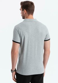Camisa polo gris con detalles negros en el cuello y las mangas. Fabricada en tejido de punto; presenta un ajuste clásico y mangas cortas.