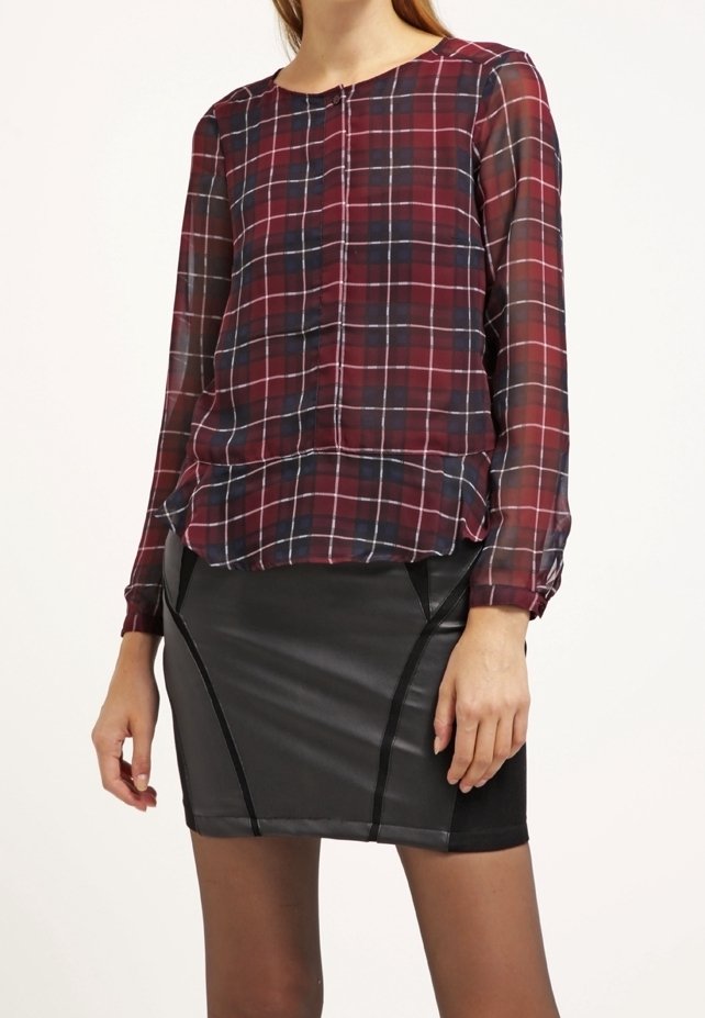 Blouse à manches longues à carreaux bordeaux et marine, en tissu transparent avec un col rond et des boutons sur le devant, associée à une jupe en cuir noir ajustée.