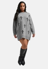 Grå stickad klänning med svarta korsmönster, oversized passform, ribbad nederkant och ärmslut, parat med knähöga svarta stövlar.