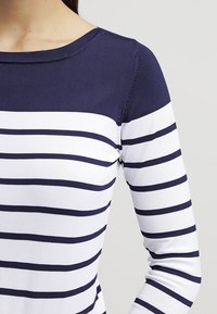 Marinblå och vit randig stickad topp, med rund halsringning och långa ärmar. Slät textur med jämna horisontella randmönster.