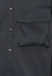 Donkerblauwe button-up overhemd met een grote borstzak. Voorzien van matte knopen en een gladde, gestructureerde stof met zichtbare stiksels.