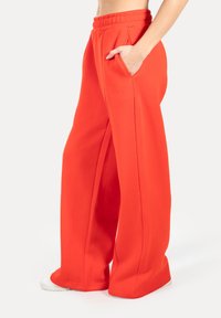 Helle rote, weit geschnittene Sweatpants aus weichem Material mit elastischem Taillenbund und seitlichen Taschen. Dezente bestickte Logodetails auf der Vorderseite.