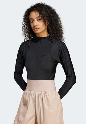 Zwarte sportieve longsleeve top met ritssluiting, textuurstof; gecombineerd met lichtroze wijde shorts met een elastische tailleband.