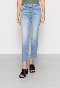 Jeans de cintura alta azul claro com fecho de cinco botões, ligeiramente alargados na bainha, combinados com sandálias de bloco de salto aberto pretas.