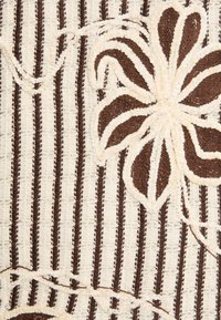 Brązowa i kremowa tkanina o fakturze z pionowymi paskami oraz dużym kwiatowym wzorem z wypukłymi detalami.