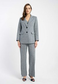 Szary garnitur skrojony na miarę z marynarką z klapami i szerokimi spodniami. Posiada dwie przednie kieszenie, czarne guziki oraz wzór strukturalny.