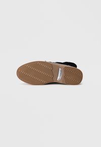 Semelle de chaussure avec un motif de semelle en zigzag et une plaque logo en métal gravée "Peter Kaiser", vue du dessous sur un fond uni.