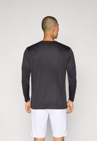Svart langermet treningsskjorte med en glatt tekstur og rund hals, båret med hvite shorts. Har ingen synlige logoer eller mønstre.