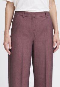 Pantaloni tailoring bordeaux con una texture liscia, design a gamba larga, tasche frontali e sottili linee verticali.