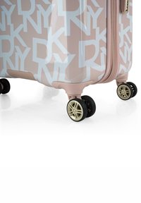 Maleta rígida de color rosa claro con un patrón de logotipo geométrico blanco; cuenta con ruedas doradas y negras; cremallera y acentos texturizados.