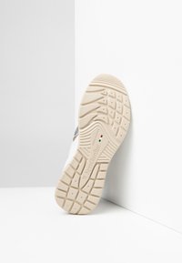 Sneaker bianco con suola in gomma beige testurizzata. Caratterizzato da una forma arrotondata, design minimalista e logo in rilievo sul lato.