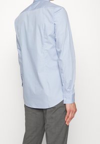 Lichtblauw overhemd met lange mouwen, een kraag met knoopsluiting, detail op het rugpand en een gladde katoenen textuur. Voorzien van manchetten met knopen en een afgeronde zoom.