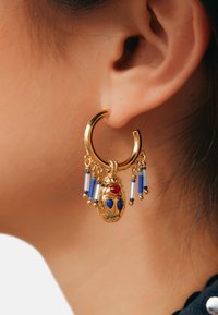 Boucle d'oreille en or avec un motif de scarabée, agrémentée de accents bleus et rouges, complétée par des perles suspendues bleues et blanches.