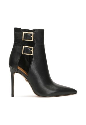 Botină din piele neagră la gleznă, cu vârf ascuțit, toc înalt tip stiletto și accente duble cu catarame aurii pe laturile tăiate. Textură netedă.