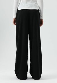 Zwarte wijde broek met een gladde textuur, voorzien van een hoge taille en zijzakken. De achterkant toont strakke lijnen en een elegante pasvorm.