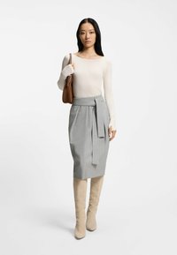Light beige long-sleeve top paired with a gray high-waisted skirt featuring a tie belt. Model wears knee-high beige boots. Smooth texture.