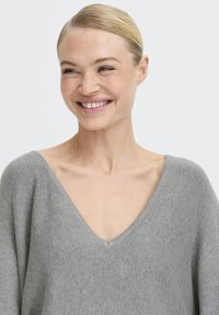 Világosszürke, oversize V nyakú pulóver, puha kötött anyagból. Lazán illeszkedő fazonnal rendelkezik, sima textúrával és minimális varrásokkal.