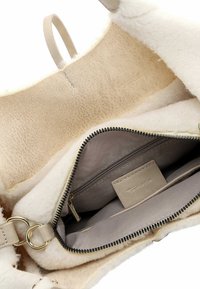 Beige väska med en mjuk, texturerad yta och ett dragkedjeinrede. Innehåller ett slätt foder med en ficka och ett märkesetikett. Guld detaljer.