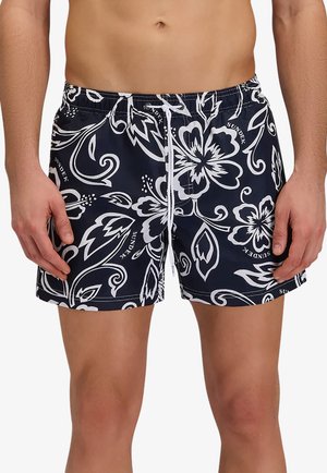 Man draagt marineblauwe zwembroek met wit bloemenpatroon en witte aantrekkoorden, getoond van taille tot halverwege de dij tegen een witte achtergrond.