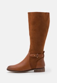 Botte marron montant en nubuck et cuir, avec un bout arrondi, une sangle au niveau de la cheville avec un accent métallique, et un petit talon en bois.