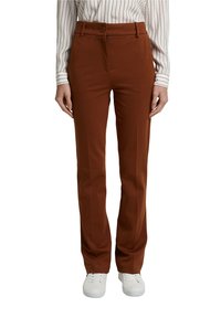 Hnědé kalhoty na míru mají rovný střih, texturovanou látku, zapínání na přední knoflík a jednotlivý klip, doplněné bílými teniskami.